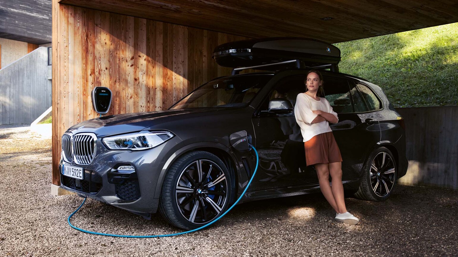 Bilde av en dame som står inntil en BMW som lader Bilde av en dame som står inntil en BMW som lader