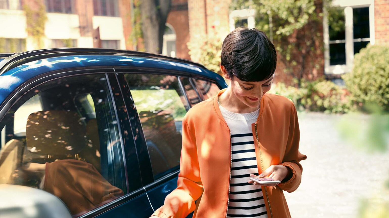 Bilde av dame som står ved siden av sin BMW og ser på mobiltelefonen